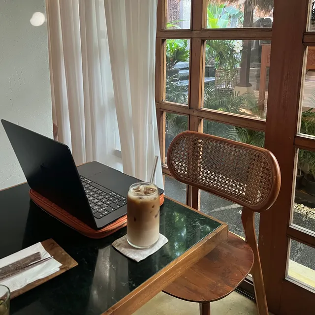 A laptop and an iced coffee on a desk beside an open window